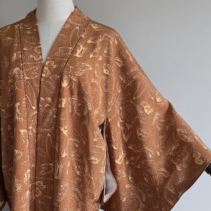May include: A brown kimono with a floral pattern is displayed on a mannequin. The kimono has wide sleeves and a V-neck. The fabric has a subtle sheen, and the floral design is in a lighter shade of brown.