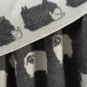 May include: A white and grey wool throw blanket with a repeating pattern of sheep and other animals. The blanket is soft and cosy, perfect for snuggling up on the sofa.