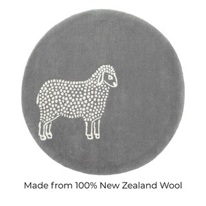 May include: A round, gray rug featuring a white sheep design. The sheep is depicted in a simple, dotted style. The text at the bottom reads "Made from 100% New Zealand Wool."