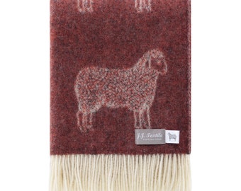May include: A folded maroon throw blanket with a sheep pattern. The blanket has a cream-colored fringe along the bottom edge. The sheep design is white and covers the blanket. The blanket has a tag that says "J.J. Textile".
