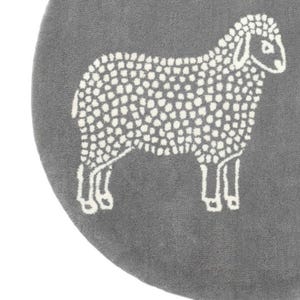 May include: A gray, round rug featuring a white sheep design. The sheep is depicted in a simple, dotted style, with a fluffy body and detailed legs. The rug has a soft, textured appearance.