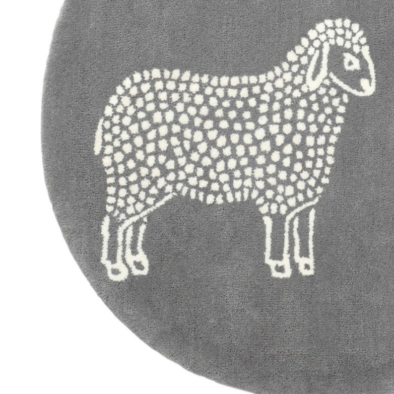 May include: A gray, round rug featuring a white sheep design. The sheep is depicted in a simple, dotted style, with a fluffy body and detailed legs. The rug has a soft, textured appearance.