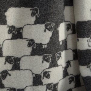 May include: A white and grey fabric with a repeating pattern of black sheep. The sheep are arranged in rows and are facing different directions.