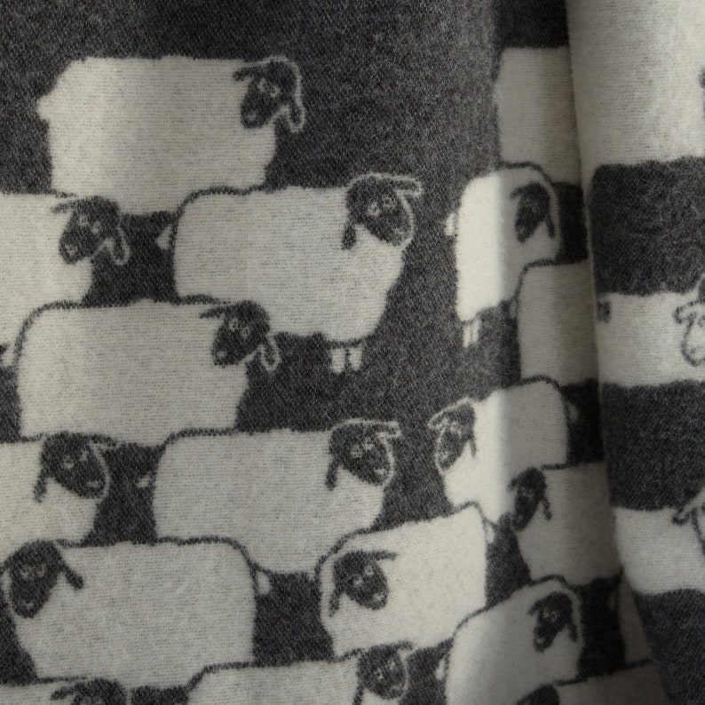 May include: A white and grey fabric with a repeating pattern of black sheep. The sheep are arranged in rows and are facing different directions.