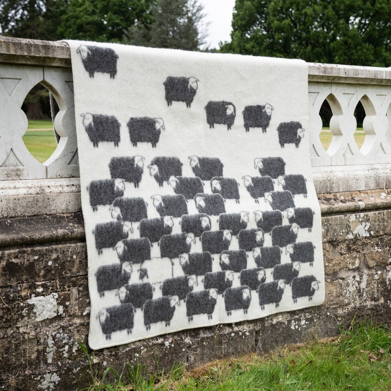 May include: A white wool throw blanket with a black sheep pattern. The blanket is draped over a stone wall.