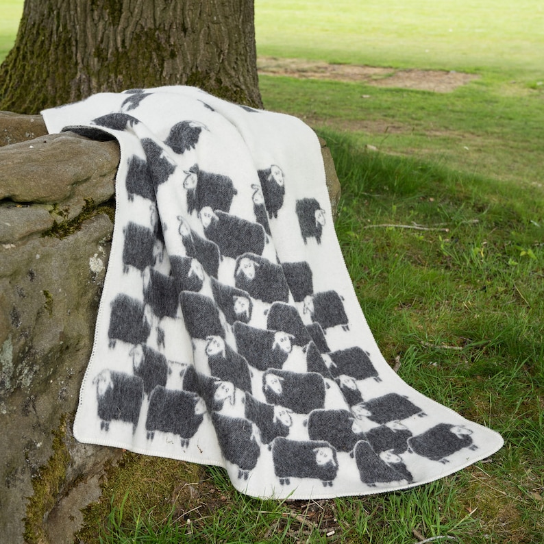 May include: A white throw blanket with a black sheep pattern. The blanket is folded and draped over a large rock.