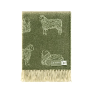 May include: A folded green blanket with a cream-colored fringe. The blanket features a repeating pattern of white sheep. The label in the bottom right corner reads "J.J. Textile".