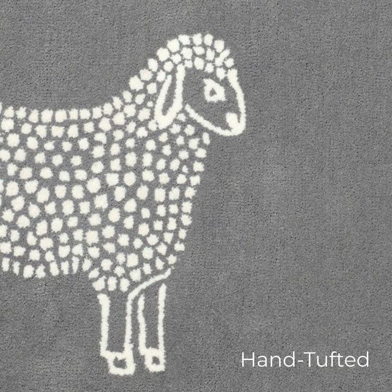 May include: A gray, hand-tufted rug featuring a white sheep design. The sheep is depicted in a simple, dotted style, with the words "Hand-Tufted" in white text at the bottom right corner.