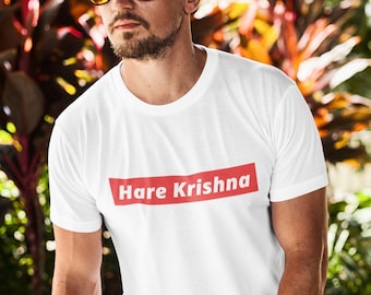 May include: White t-shirt with a red box that says "Hare Krishna" printed on the front. The person is wearing black pants and sunglasses.