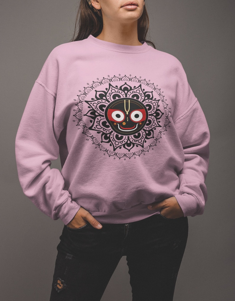 May include: A pink sweatshirt with a black and white mandala design featuring a black face with red eyes and a gold symbol on the front.