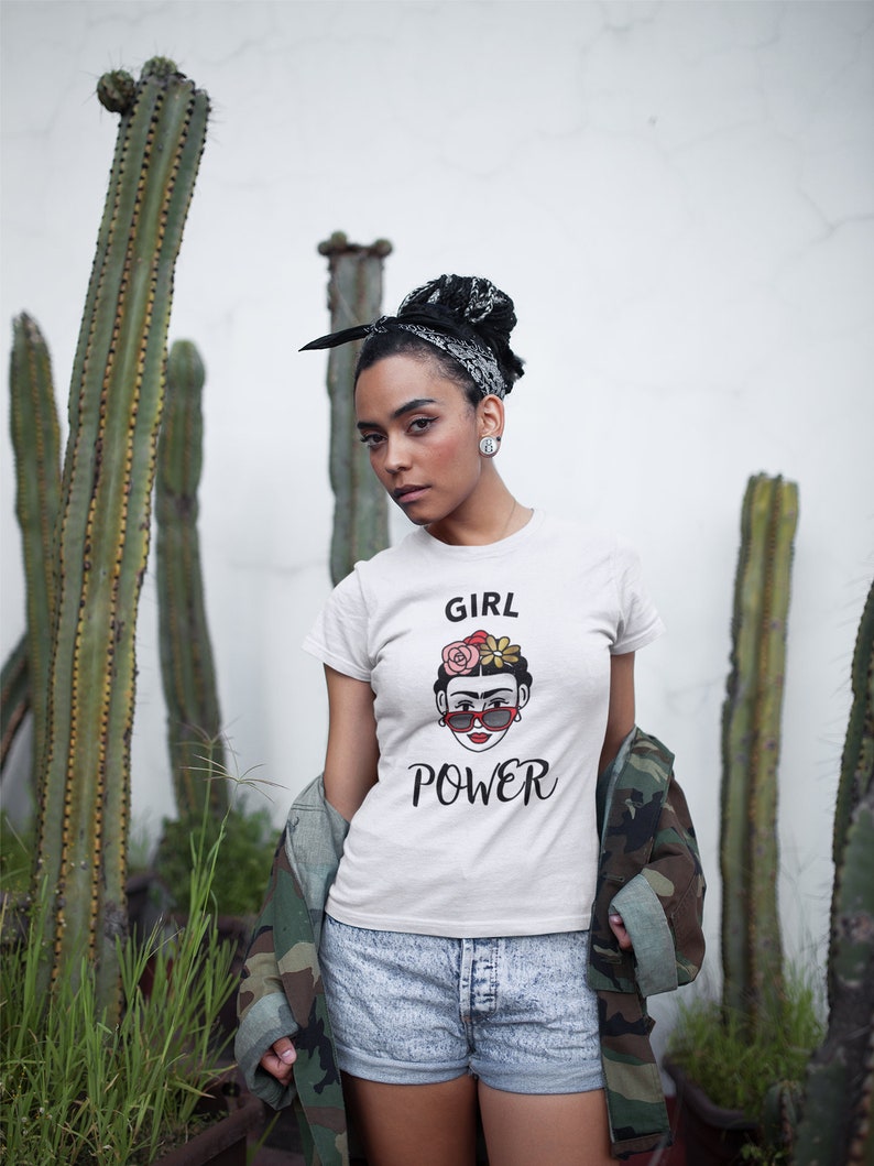 May include: White t-shirt with a graphic of Frida Kahlo wearing sunglasses and flowers in her hair. The text "GIRL POWER" is printed below the graphic.