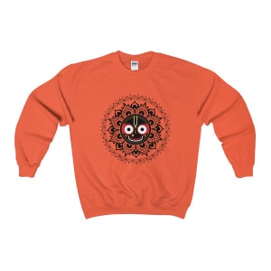 May include: Orange sweatshirt with a black and white mandala design featuring a black face with red eyes and a white dot in the centre.