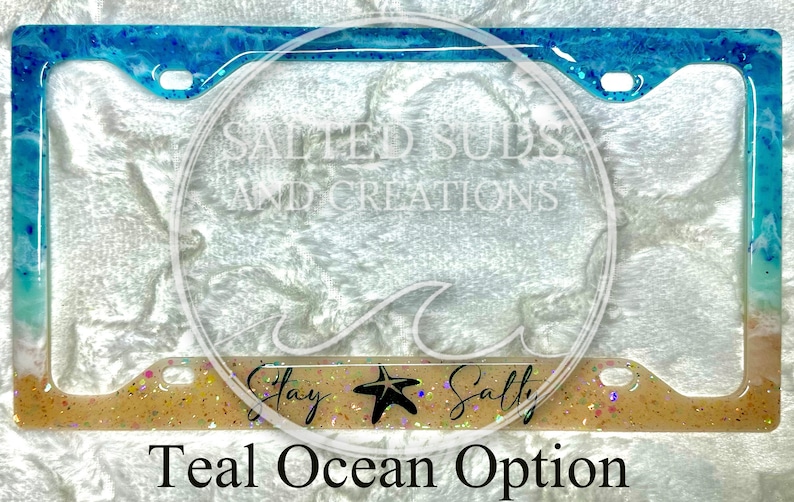 Pu&ograve; includere: Cornice per targa di colore blu-verde e bianco a tema oceanico, con glitter e una stella marina. La cornice ha il testo "Stay Salty" in basso.