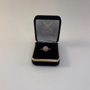 May include: A pink ring with a round stone in a black velvet ring box.