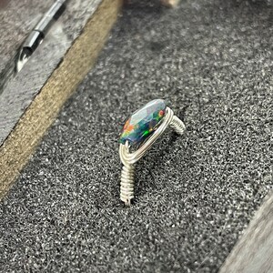 May include: A silver wire wrapped ring with a dark green, black, and red opal gemstone.