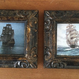 May include: Two framed pictures of sailing ships on the ocean. The frames are dark brown with gold accents. The pictures are in a vintage style.