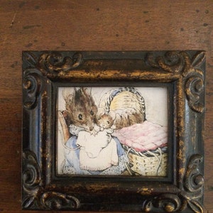May include: A framed illustration featuring a mother mouse and her children. The artwork is set in a decorative, dark brown frame with gold accents. The image depicts a cozy scene with soft colors and detailed linework.