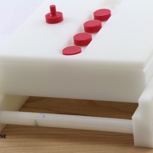 May include: White plastic soap making mold with a red knob and five red circles. The mold is on a wooden surface.