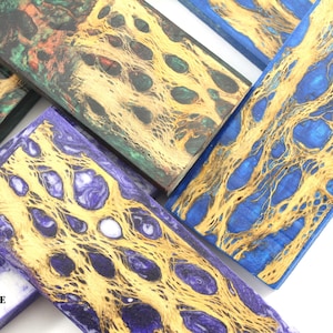 May include: Close-up of several rectangular wood pieces with unique patterns. The pieces feature a mix of colors, including blue, purple, green, and yellow, with intricate, organic designs. The wood grain is visible, adding to the natural aesthetic.