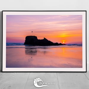 May include: A silhouette of a rocky island with a flag at the peak, reflected in the calm water of a beach at sunset. The sky is a vibrant mix of pink, orange, and purple.