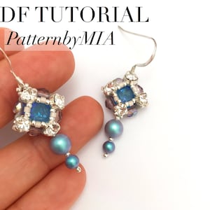 May include: A pair of silver dangle earrings with a blue and white cube-shaped bead and iridescent blue and purple beads hanging from the bottom. The earrings are on a white background. PDF TUTORIAL PatternbyMIA