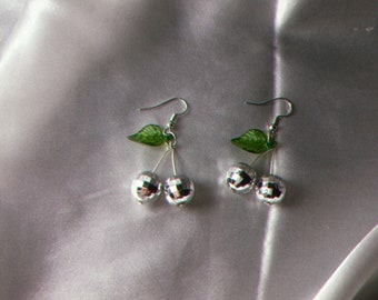 May include: Silver disco ball cherry earrings with green leaves.