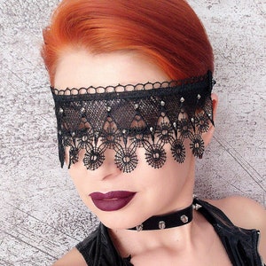 May include: A black lace eye mask with silver embellishments. The mask has a scalloped edge and covers the eyes and forehead.