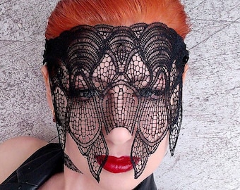 May include: A black lace mask with a delicate floral pattern covers the eyes of a person with bright red hair. The mask is worn over the face, leaving the nose and mouth visible. The person is wearing a black leather jacket.