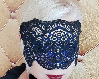 May include: A black lace eye mask with blue rhinestones. The mask is delicate and intricate, with a scalloped edge.