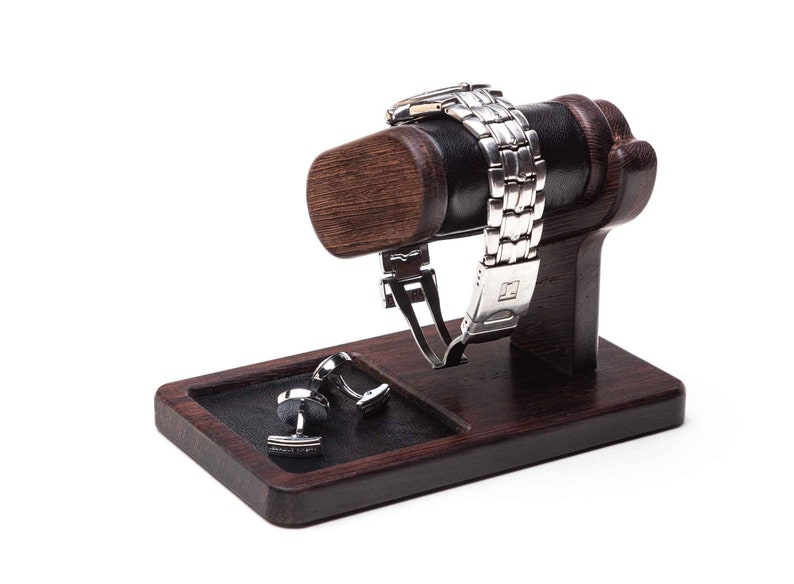May include: A wooden watch and cufflinks stand with a black leather watch holder and a black leather cufflinks tray. The stand is dark brown and has a smooth finish.