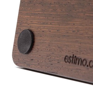 May include: Close-up of a dark brown wooden surface with a black round rubber foot. The surface has a wood grain pattern and the text 'estimo.co' is engraved on the bottom right corner.