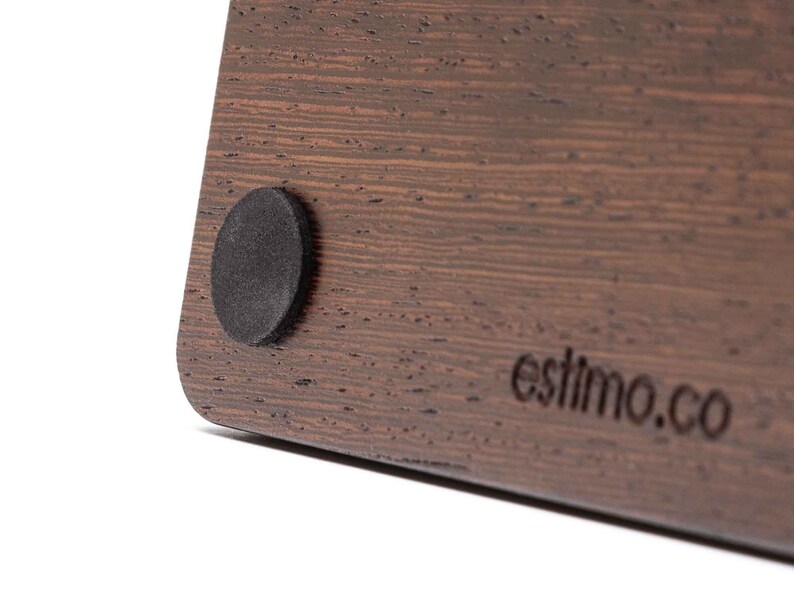 May include: Close-up of a dark brown wooden surface with a black round rubber foot. The surface has a wood grain pattern and the text 'estimo.co' is engraved on the bottom right corner.