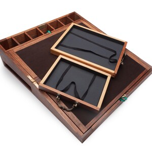 Op de afbeelding: Een houten sieradendoos met een donkerbruin vilt interieur en twee uitneembare trays. De doos heeft een scharnierend deksel, kleine compartimenten en een messing handvat. De buitenkant is van donker hout.