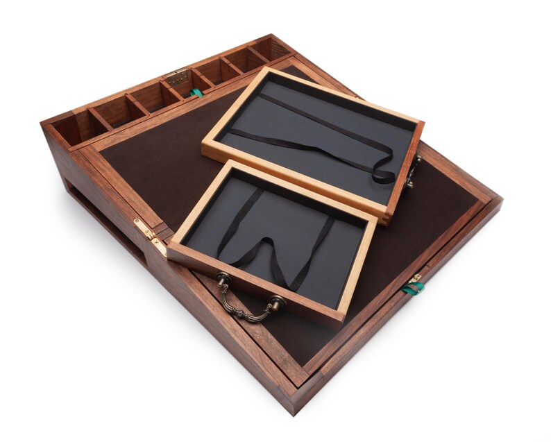 Op de afbeelding: Een houten sieradendoos met een donkerbruin vilt interieur en twee uitneembare trays. De doos heeft een scharnierend deksel, kleine compartimenten en een messing handvat. De buitenkant is van donker hout.