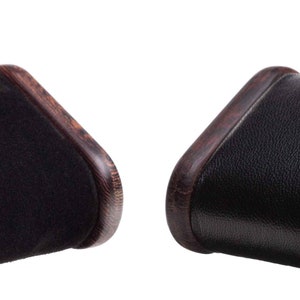 May include: Two black suede watch cushions with brown wood frames. The cushions are rectangular and have rounded edges. The wood frames have a dark brown finish and a wood grain pattern.