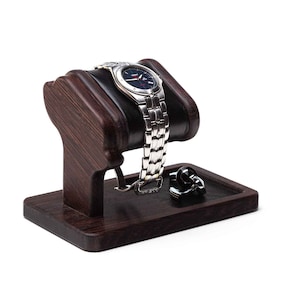 May include: A dark brown wooden watch stand with a black leather cushion to hold a watch. A pair of cufflinks are on the stand's tray.