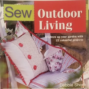 May include: The cover of a book titled "Sew Outdoor Living" features a white bench with a patterned pillow and cups. The book promises 22 colorful projects. Additional images show a teepee, heart-shaped decorations, and a picnic set.