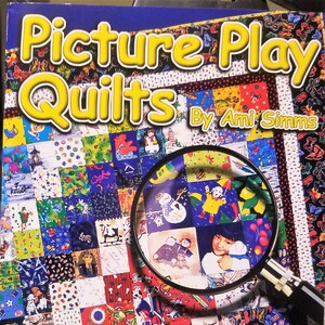 May include: A book titled "Picture Play Quilts" by Ami Simms. The cover features a colorful patchwork design with various images and a magnifying glass. Includes 10 free plastic templates.
