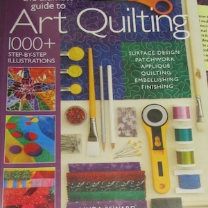 May include: A book titled "Art Quilting" with the text "1000+ Step-by-Step Illustrations." The image includes quilting tools like scissors, rotary cutter, brushes, pins, and spools of thread. Fabric swatches and the author's name are also visible.