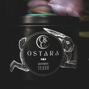 Könnte beinhalten: Eine schwarze Blechkerze mit einer weißen Hasenillustration und dem Text "C&C Ostara Doc Jasmine Ylang Ylang".
