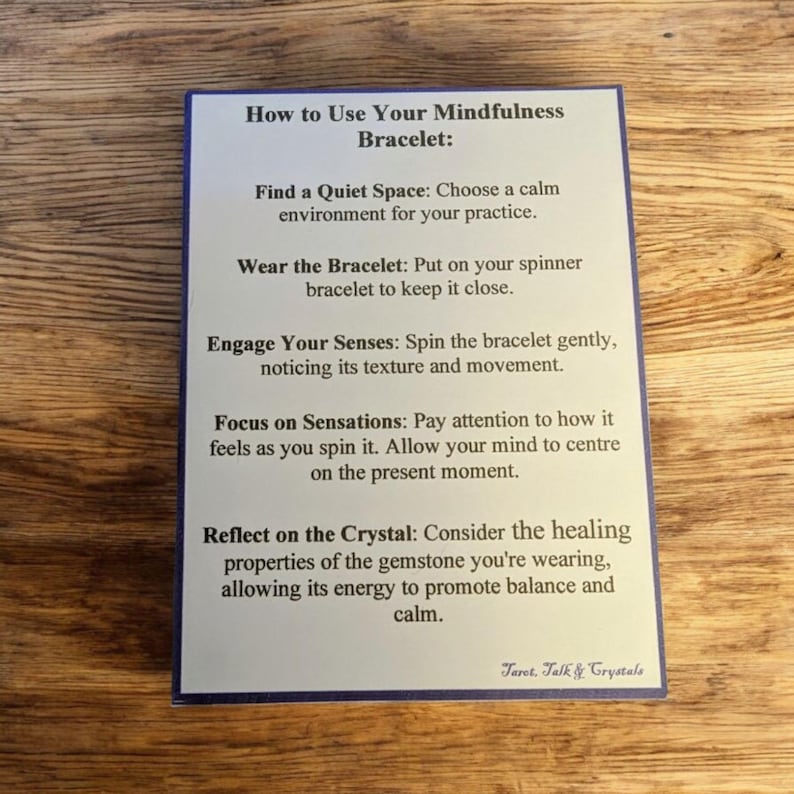 May include: A white card with blue text explaining how to use a mindfulness bracelet. The card includes instructions on finding a quiet space, wearing the bracelet, engaging your senses, focusing on sensations, and reflecting on the crystal. The card also includes the text "Taret. Talk & Crystals".