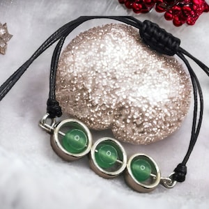 May include: A black leather bracelet with three green jade beads in silver settings. The bracelet is tied with a knot and has a decorative silver clasp.