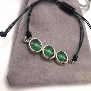 May include: A green stone bracelet with three round stones set in silver. The bracelet is made with black cord and has a silver clasp.