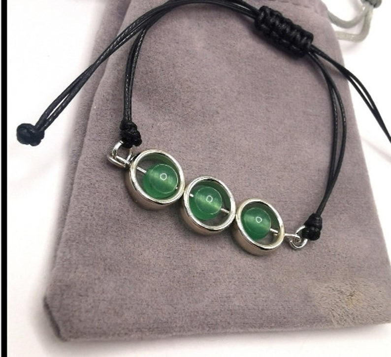 May include: A green stone bracelet with three round stones set in silver. The bracelet is made with black cord and has a silver clasp.