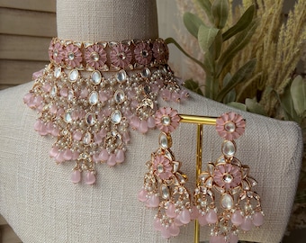 May include: A pink and gold bridal necklace and earrings set with floral accents and pearl detailing.