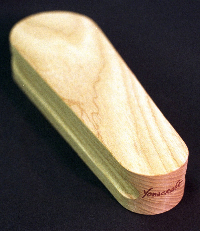 May include: A wooden, light brown, coffin-shaped box with a rounded top and a slightly curved bottom. The box has a red inscription on the bottom that reads "Yonecrafts".