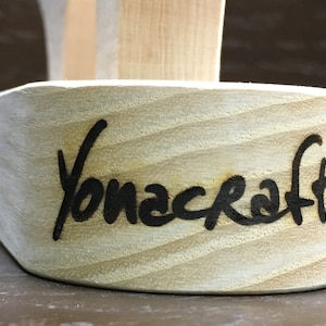 Puede incluir: Primer plano de un objeto de madera con la palabra "Yonacraft" grabada en la parte inferior.