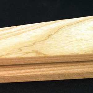 May include: A wooden tool for shaping leather, with a curved top and a flat bottom. The tool is made of light wood with a natural grain.