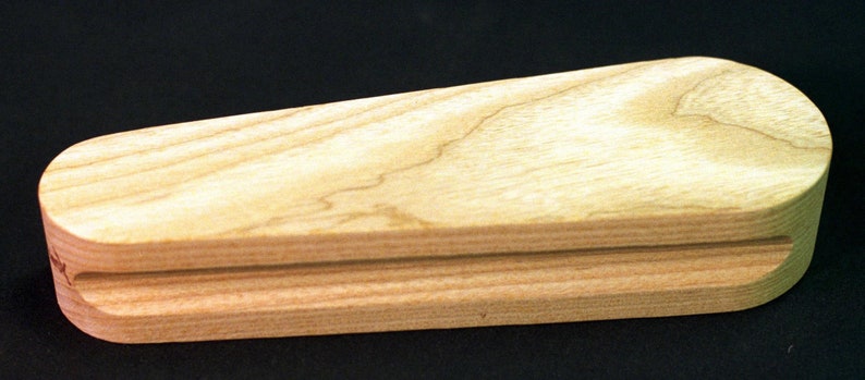 May include: A wooden tool for shaping leather, with a curved top and a flat bottom. The tool is made of light wood with a natural grain.