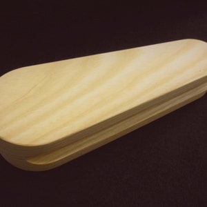 May include: A wooden box with a rounded top and a smooth, light brown finish. The box is made of two pieces of wood that are joined together.